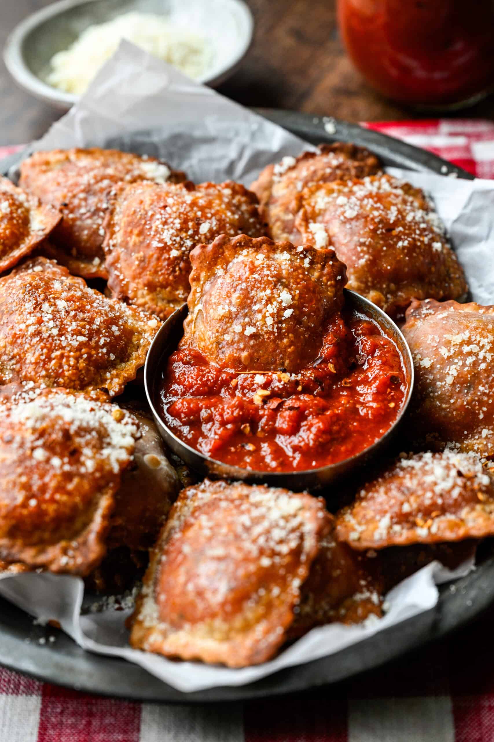 Close-up of a crispy homemade pizza roll dipped in a bowl of pizza sauce, surrounded by more pizza rolls dusted with parmesan.