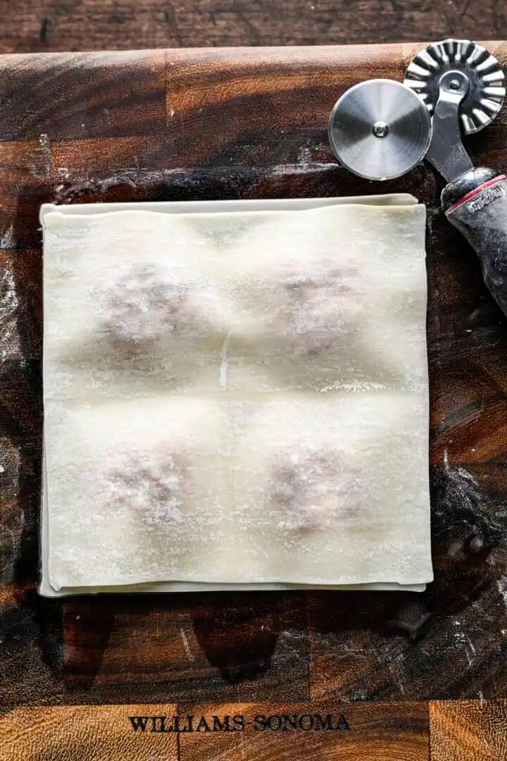 A second egg roll wrapper laid over the filling and pressed down around the four mounds to seal.