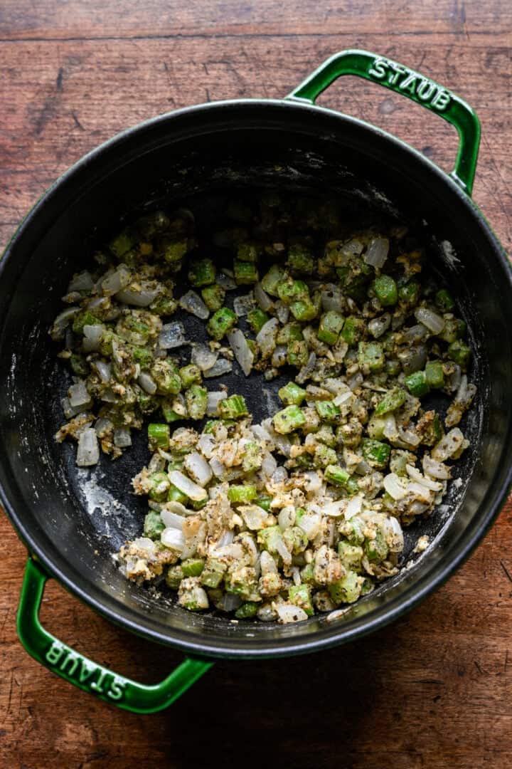 Overhead view of sautéed onion and celery coated in flour, garlic and Italian seasoning in a green Dutch oven