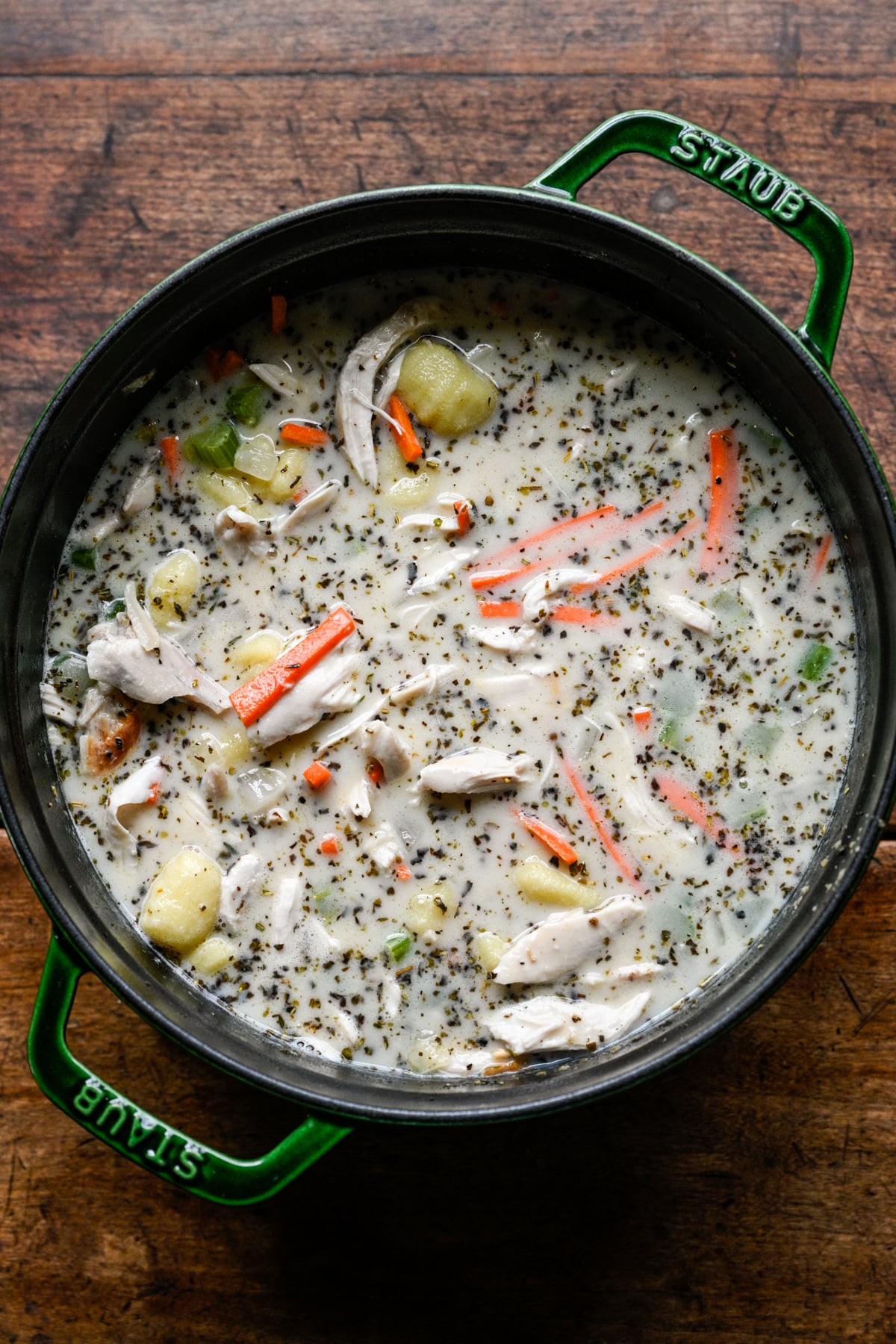 Overhead view of shredded chicken, gnocchi and matchstick carrots simmering in creamy broth in a green Dutch oven