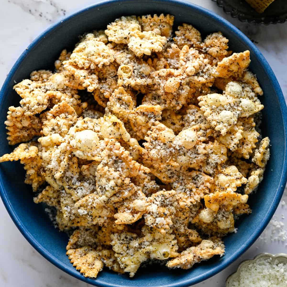 Overhead view of a blue bowl of puffed pasta dusted with parmesan and cracked pepper.