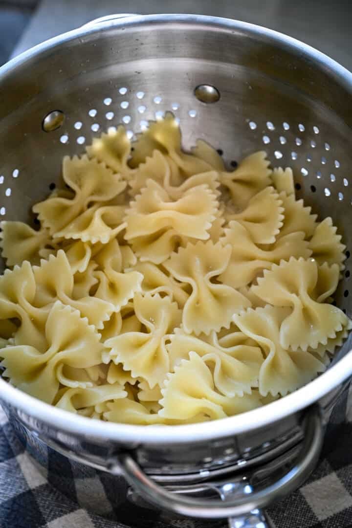 Overhead view of cooked bow tie pasta draining in a metal colander set in a pot.