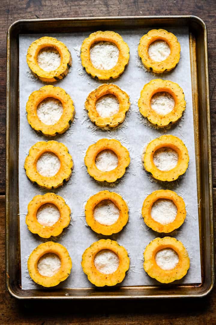 Overhead view of seasoned delicata squash rings on a parchment lined sheet pan, each filled with grated parmesan.