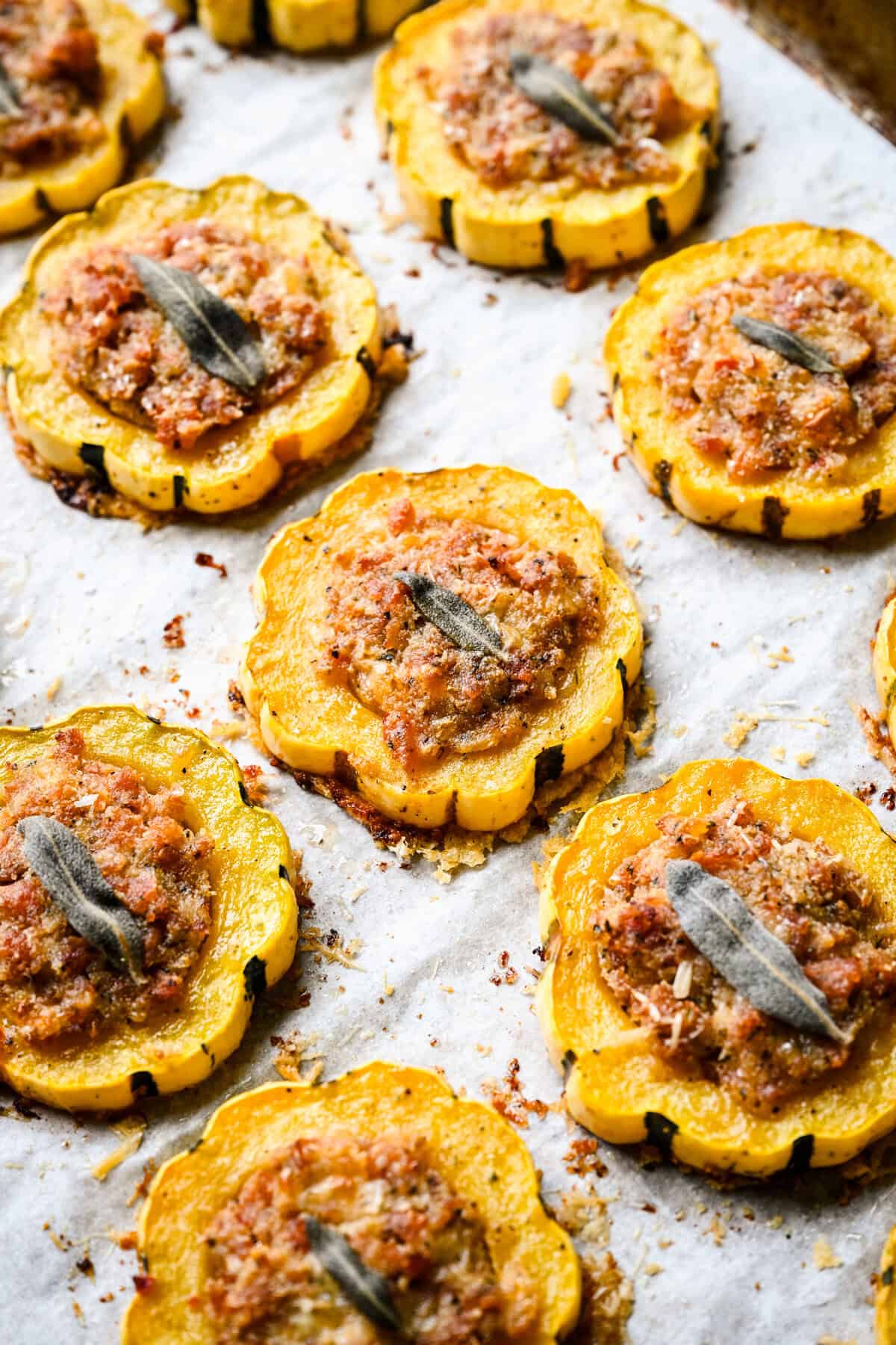 45 degree view of baked sausage stuffed delicata squash rings on a parchment lined pan.