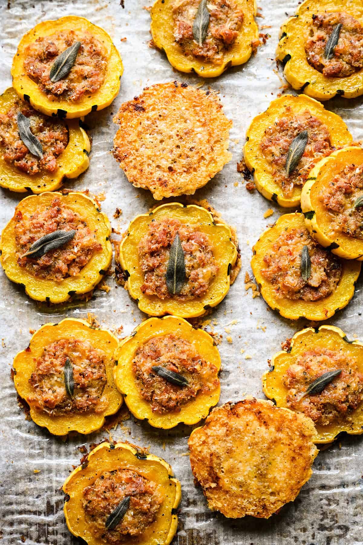 Overhead view of stuffed delicata squash rings and two parmesan crisps on a parchment lined pan.