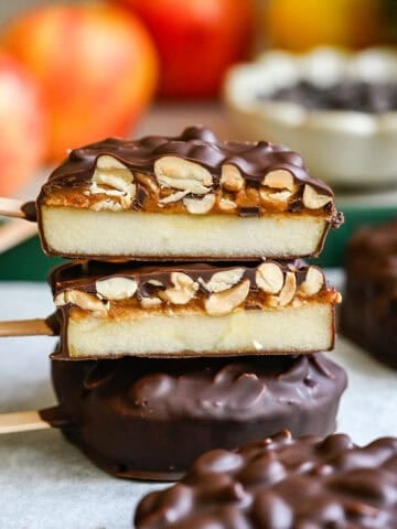 Front view of a stack of chocolate covered apple slices cut in half, showing the apple, date spread and peanut layers inside.