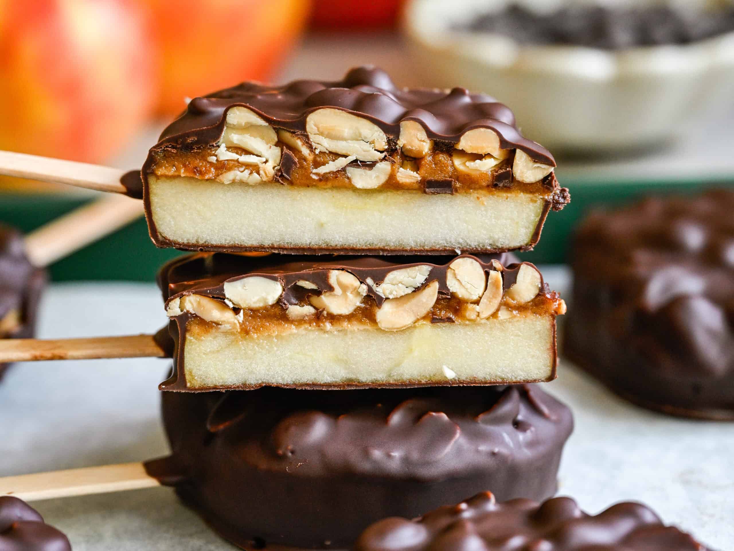 Close up front view of two cut chocolate covered apple slices, showing the apple, date spread and peanut layers.