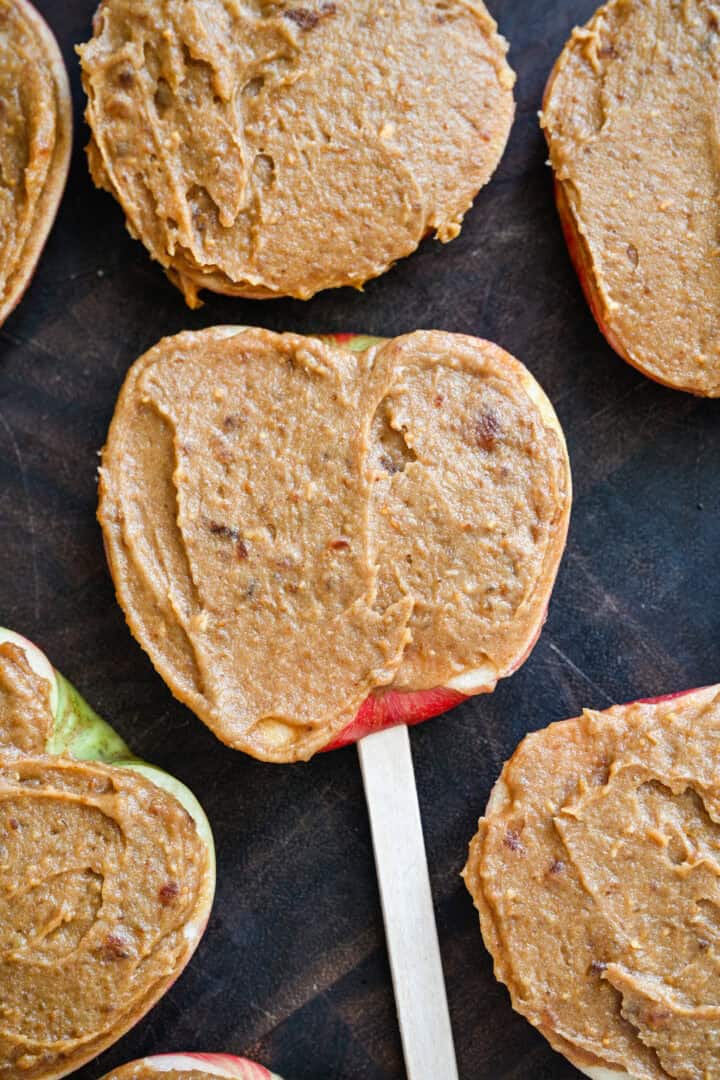 Close up view of apple slices on popsicle sticks spread with a layer of peanut butter date spread.