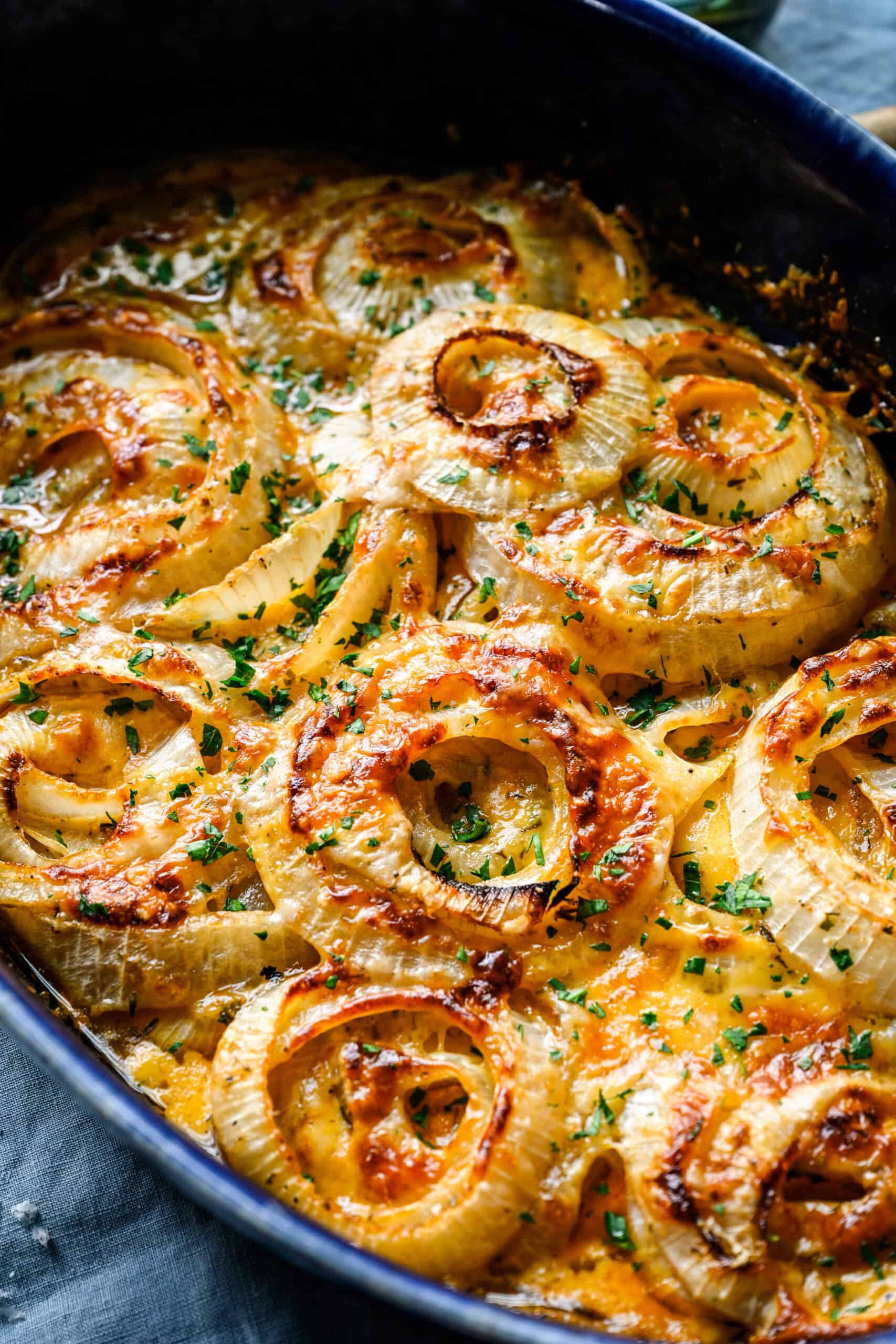 45 degree close up of Tennessee onions, cheese deeply golden and bubbled over the onion rings with chopped parsley on top.