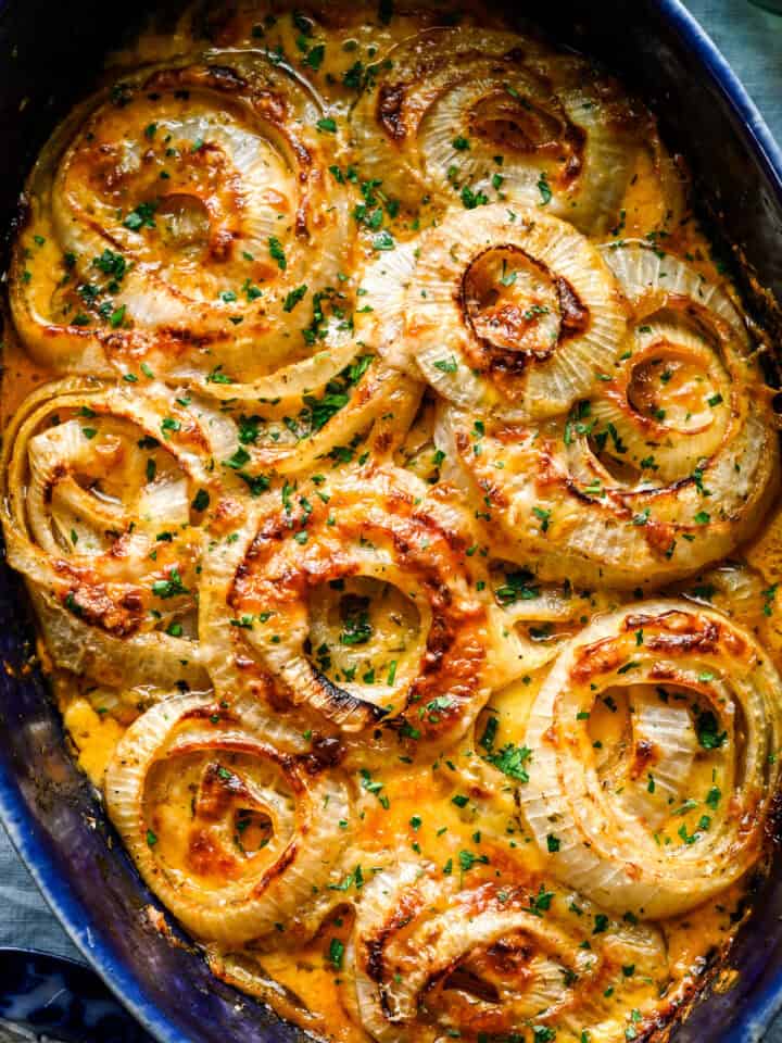 Overhead close up of Tennessee onions in a blue baking dish, cheese deeply browned on the onion rings and sprinkled with chopped parsley.